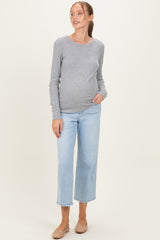 woman wearing a gray long sleeve maternity top and light blue cropped jeans, gently cradling her baby bump