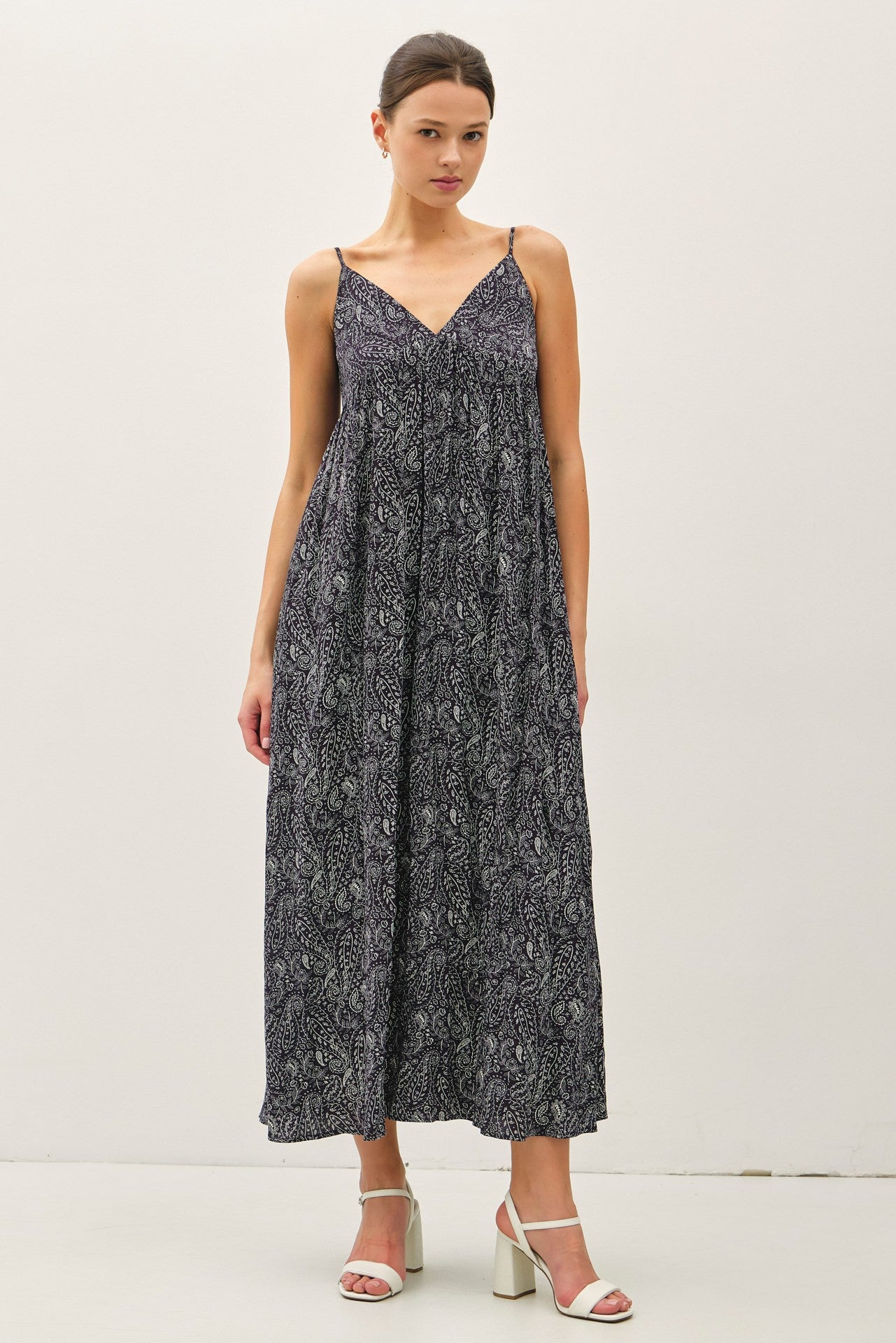 woman wearing a navy blue maxi dress with a patterned design and thin straps, standing against a plain background