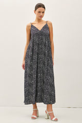 woman wearing a navy blue maxi dress with a patterned design and thin straps, standing against a plain background