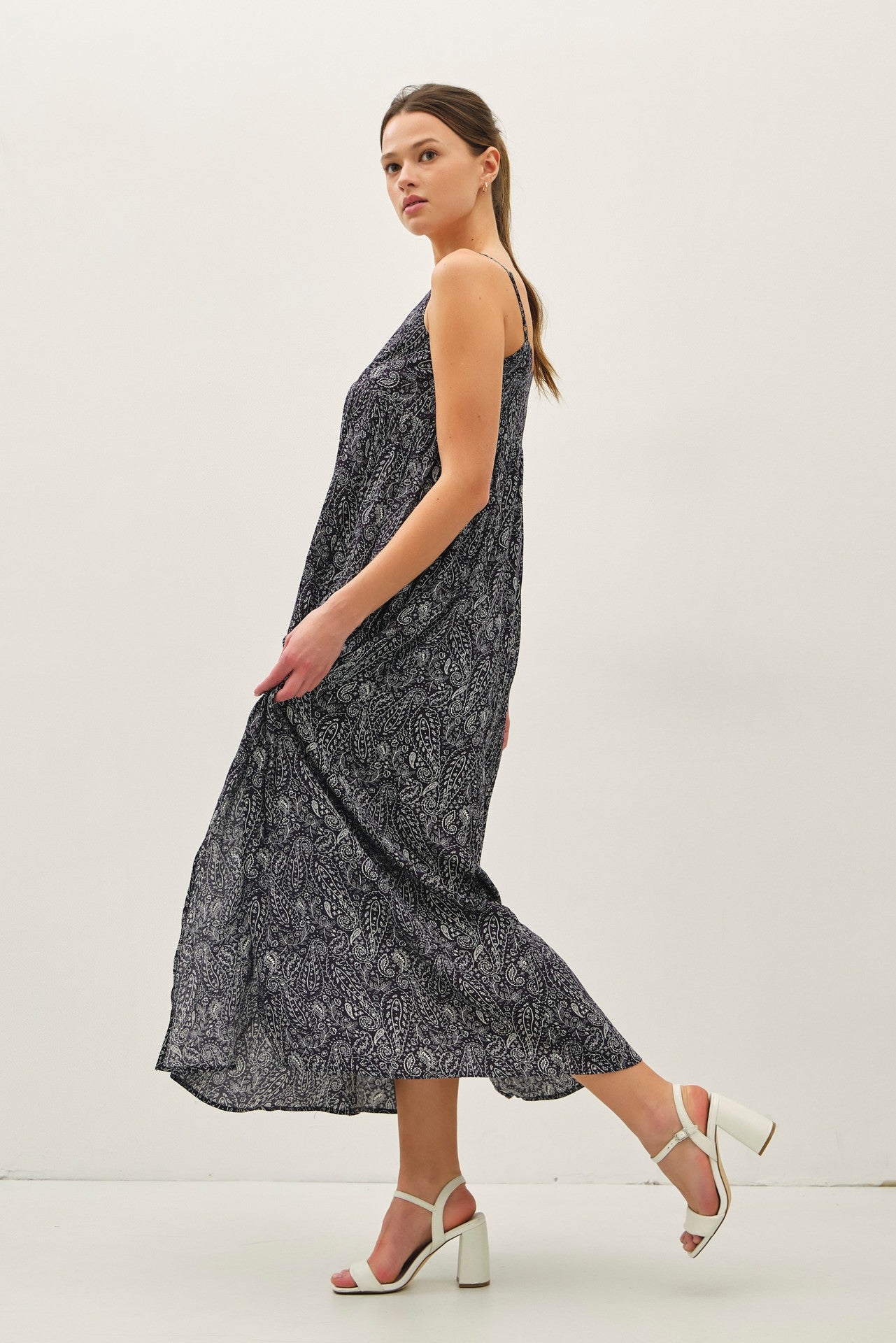 woman wearing a flowy navy blue maxi dress with a paisley print and white block-heeled sandals