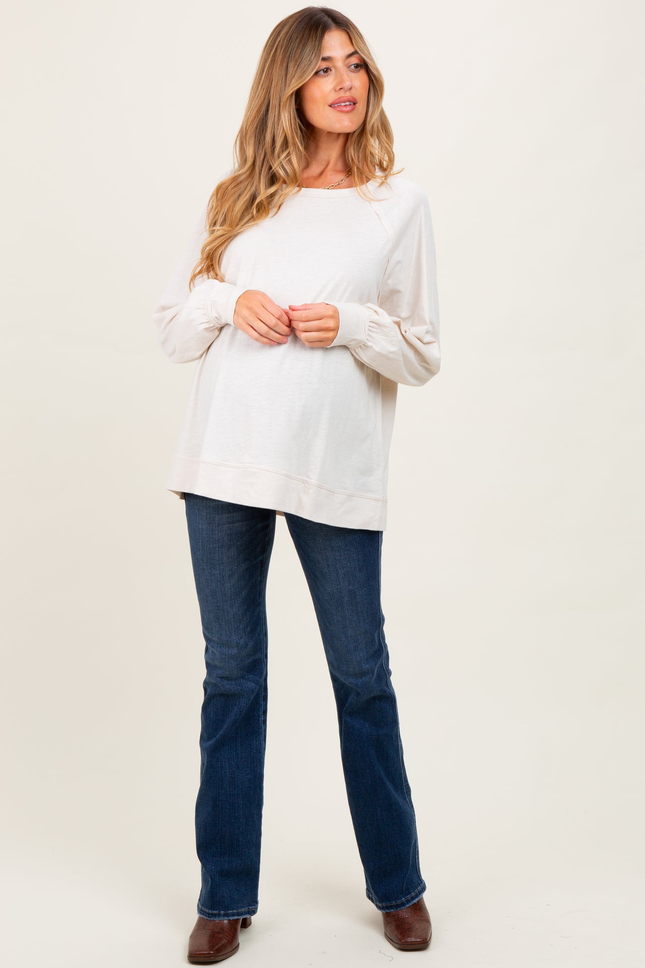 woman wearing a light beige maternity top and dark jeans, showing a baby bump