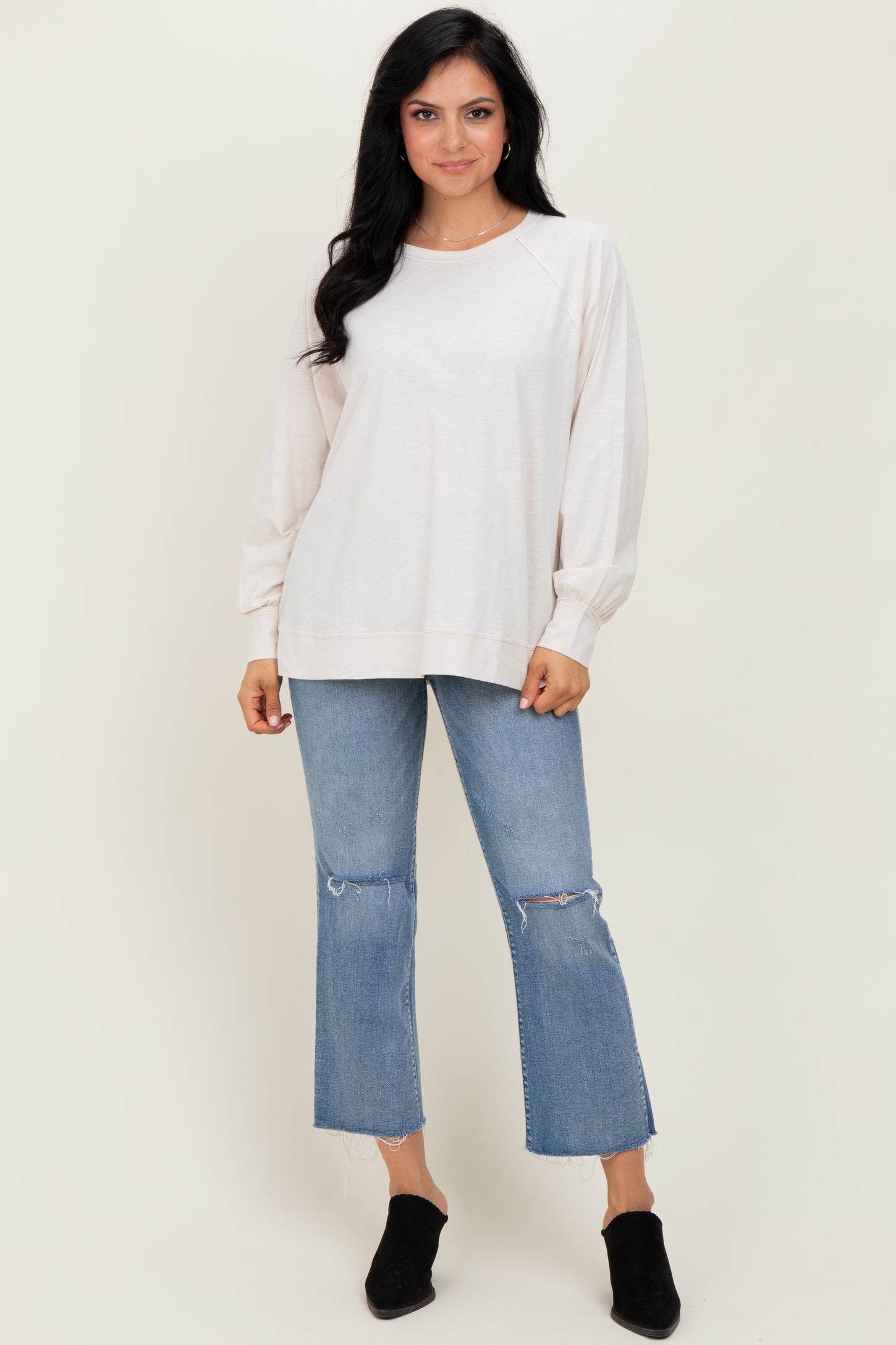 woman wearing a light beige oversized sweatshirt with balloon sleeves and blue distressed cropped jeans
