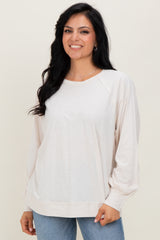 woman wearing a soft beige long sleeve top with raglan sleeves and elastic cuffs, smiling against a neutral background