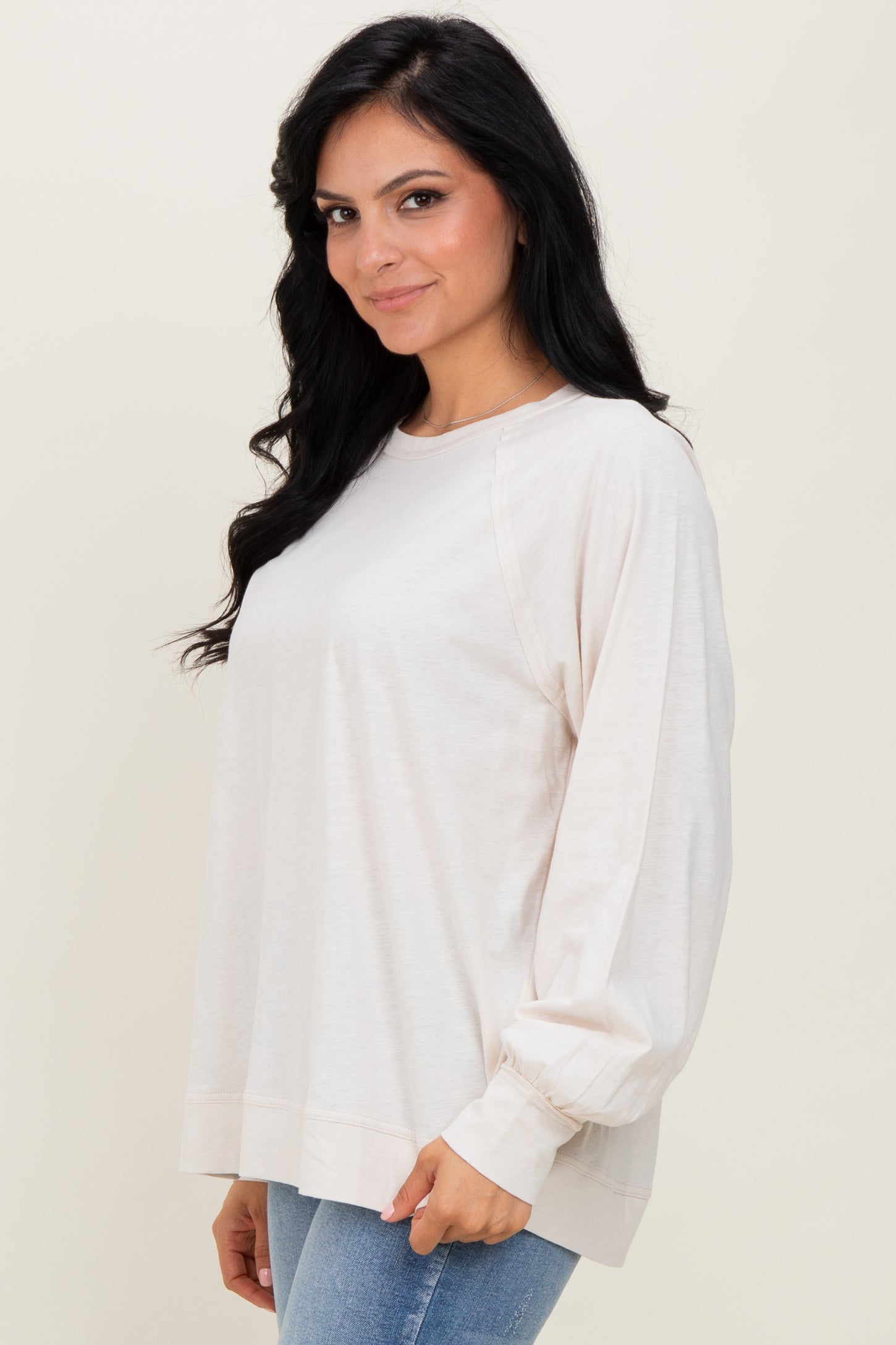 woman wearing a light beige long sleeve top with relaxed fit and balloon sleeves paired with blue jeans