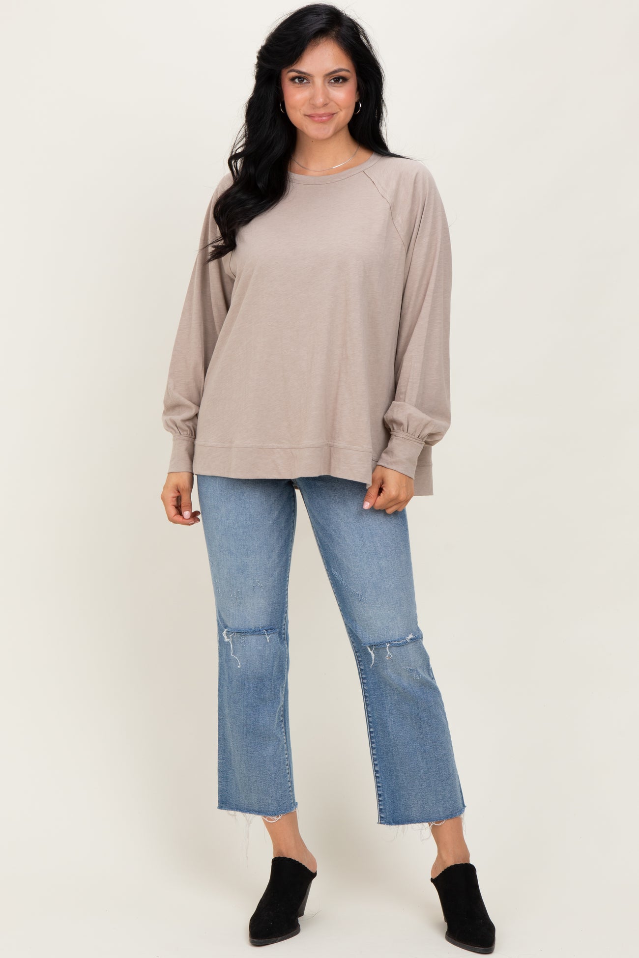 woman wearing a beige long sleeve loose top with balloon sleeves paired with light blue cropped jeans and black mules