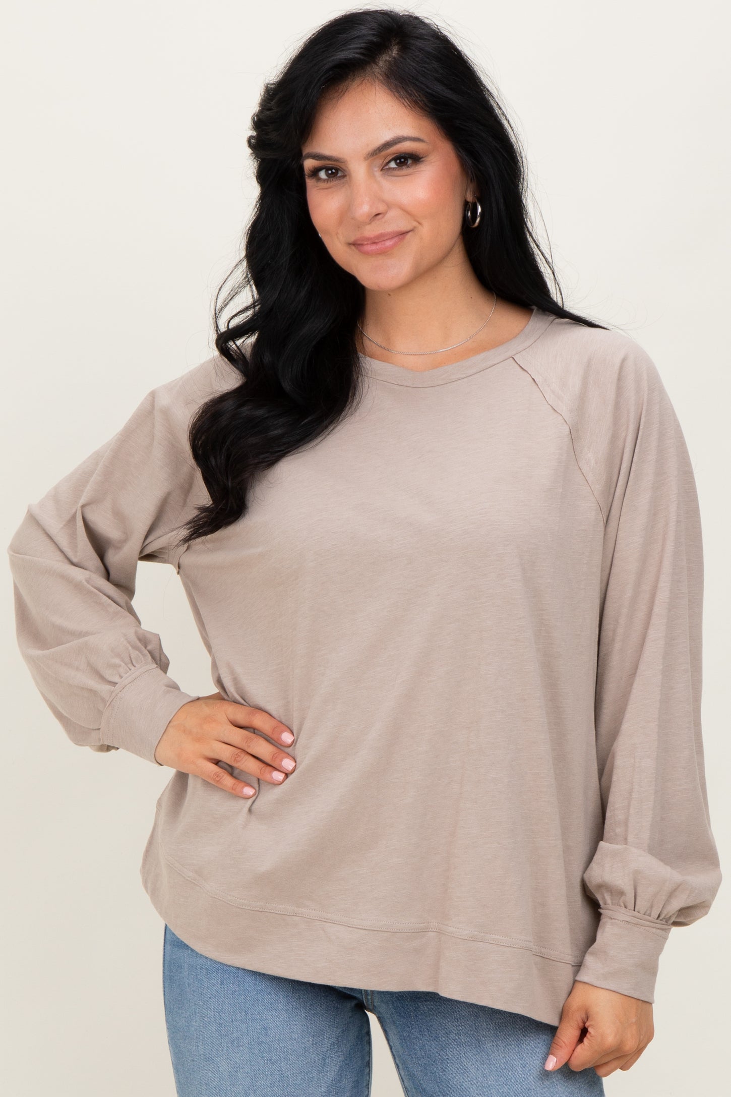 woman wearing a taupe oversized long sleeve top with raglan sleeves and a relaxed fit, paired with light blue jeans