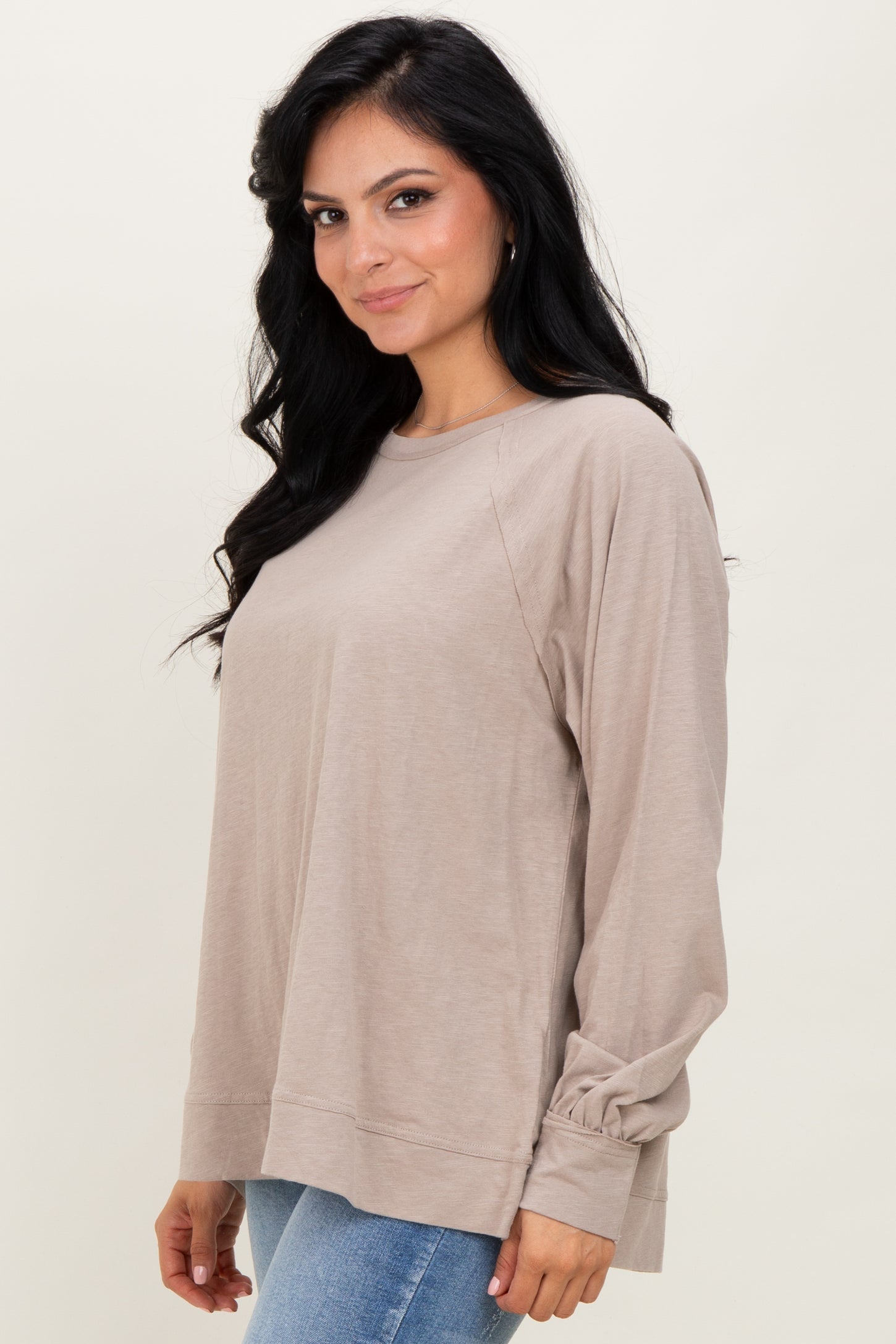 woman wearing a light beige long sleeve top with gathered sleeves and a relaxed fit, paired with blue jeans