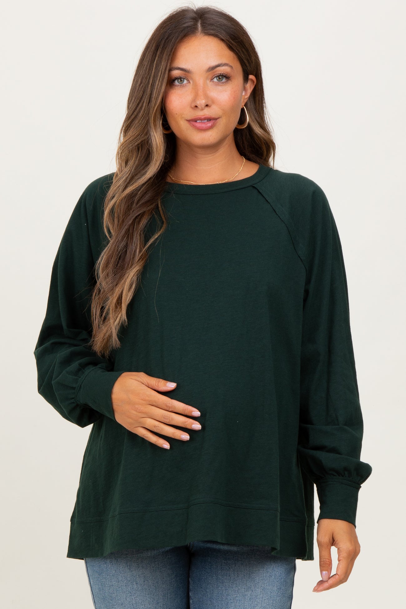 woman wearing a dark green long sleeve maternity top and holding her baby bump