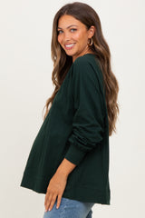 woman wearing a dark green long sleeve maternity top with a relaxed fit and visible baby bump