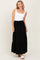 woman wearing a white square neck tank top and a black tiered maxi skirt, standing and smiling