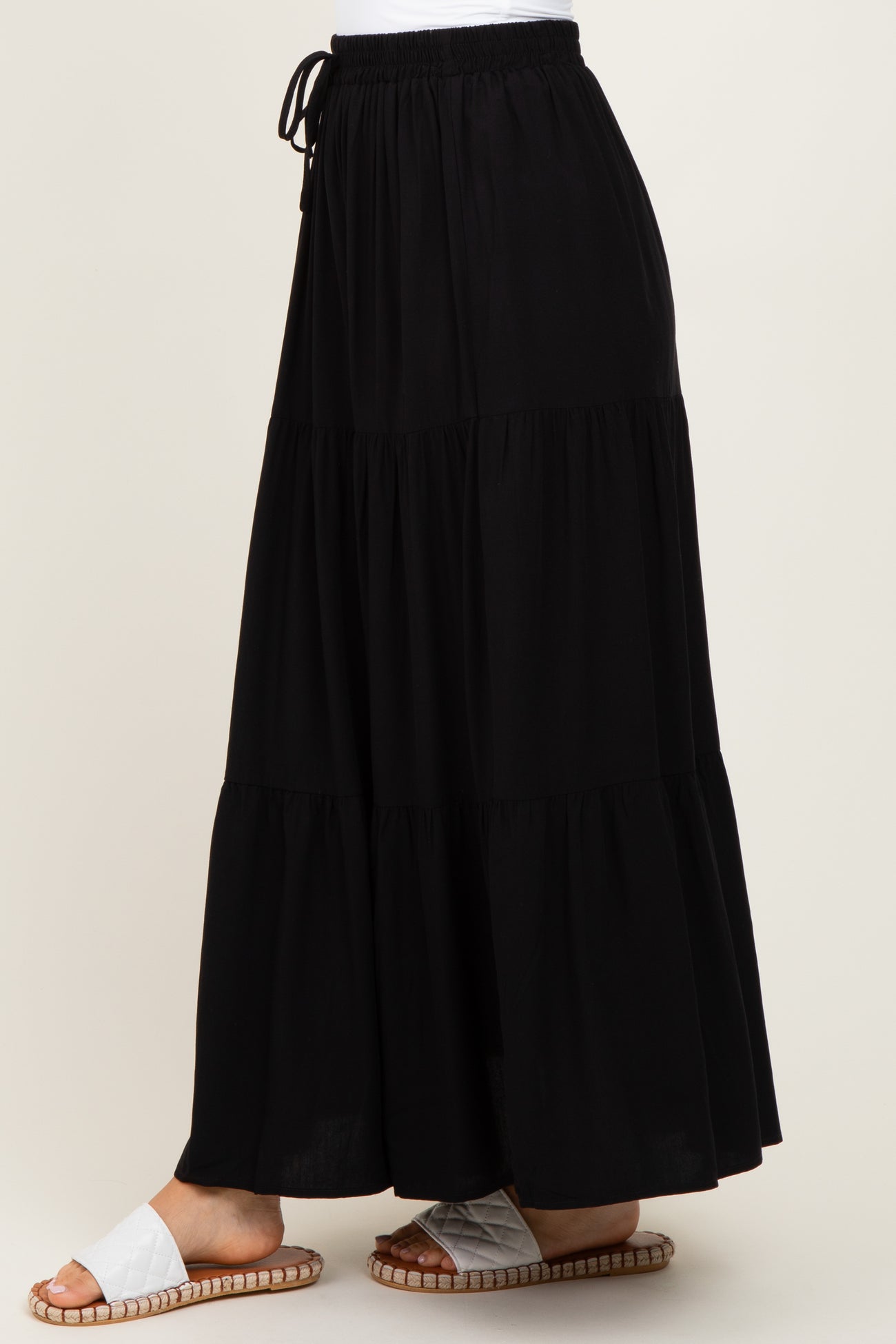 woman wearing a black tiered maxi skirt with an elastic waistband and drawstring, paired with white sandals