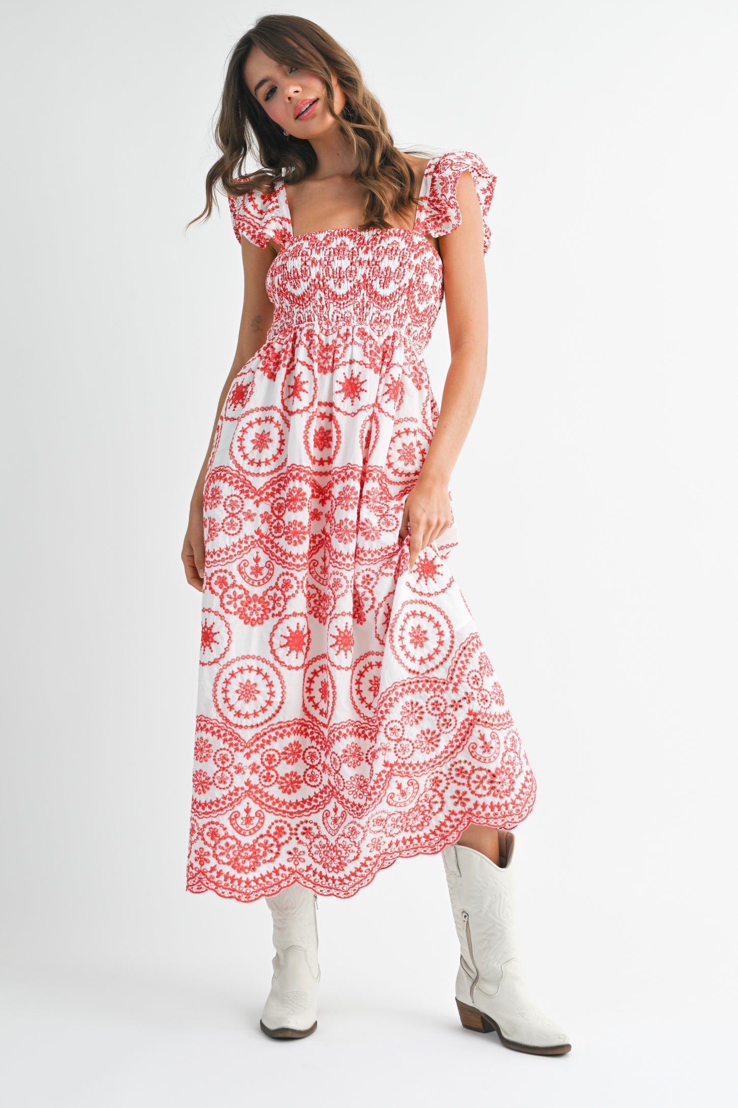 woman wearing a red and white patterned maxi dress with ruffled sleeves and holding the skirt while wearing white boots