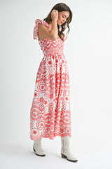 woman wearing a red and white patterned maxi dress with ruffled sleeves and white cowboy boots