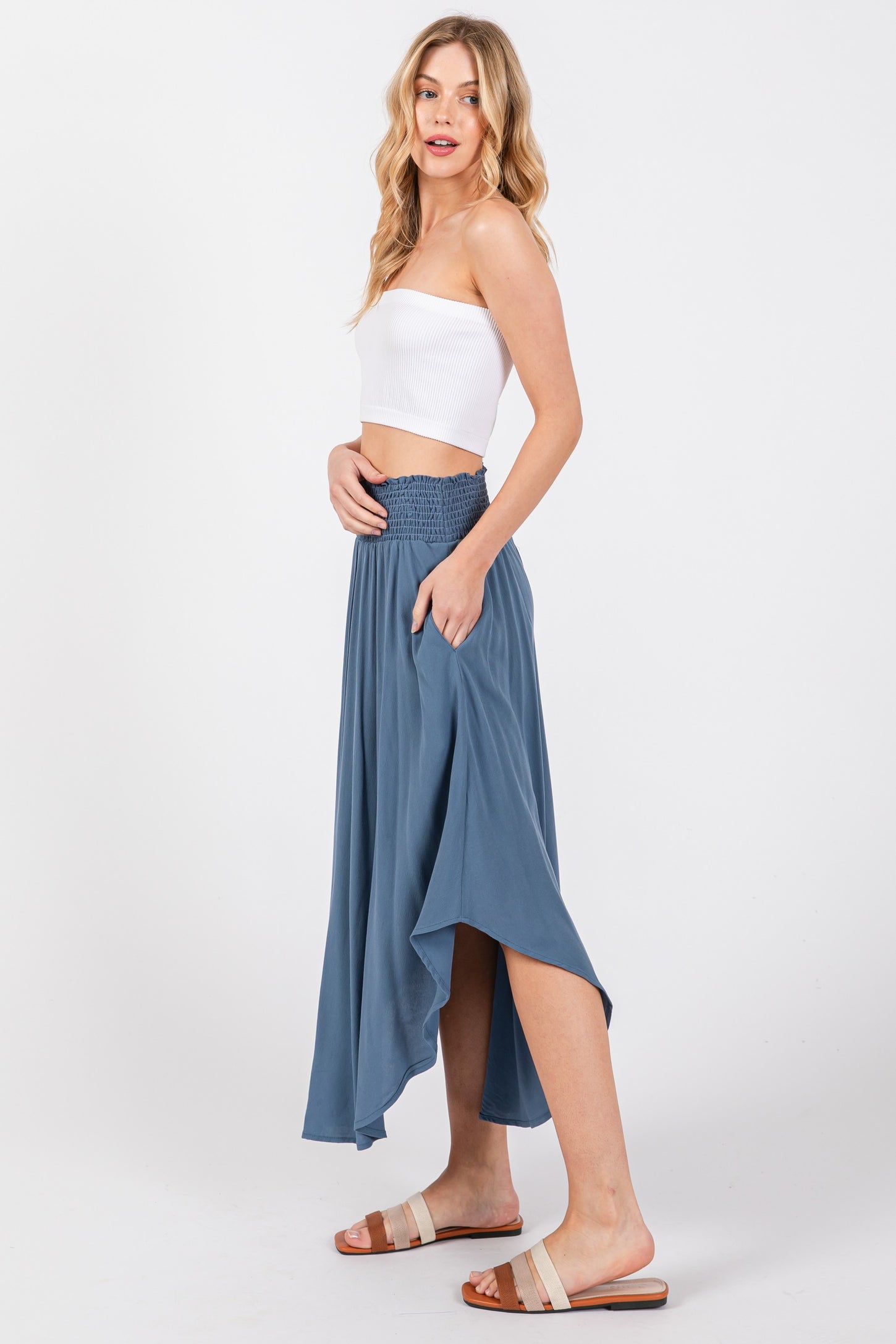 woman wearing a white strapless top and a flowy blue maxi skirt with a smocked waistband and pockets