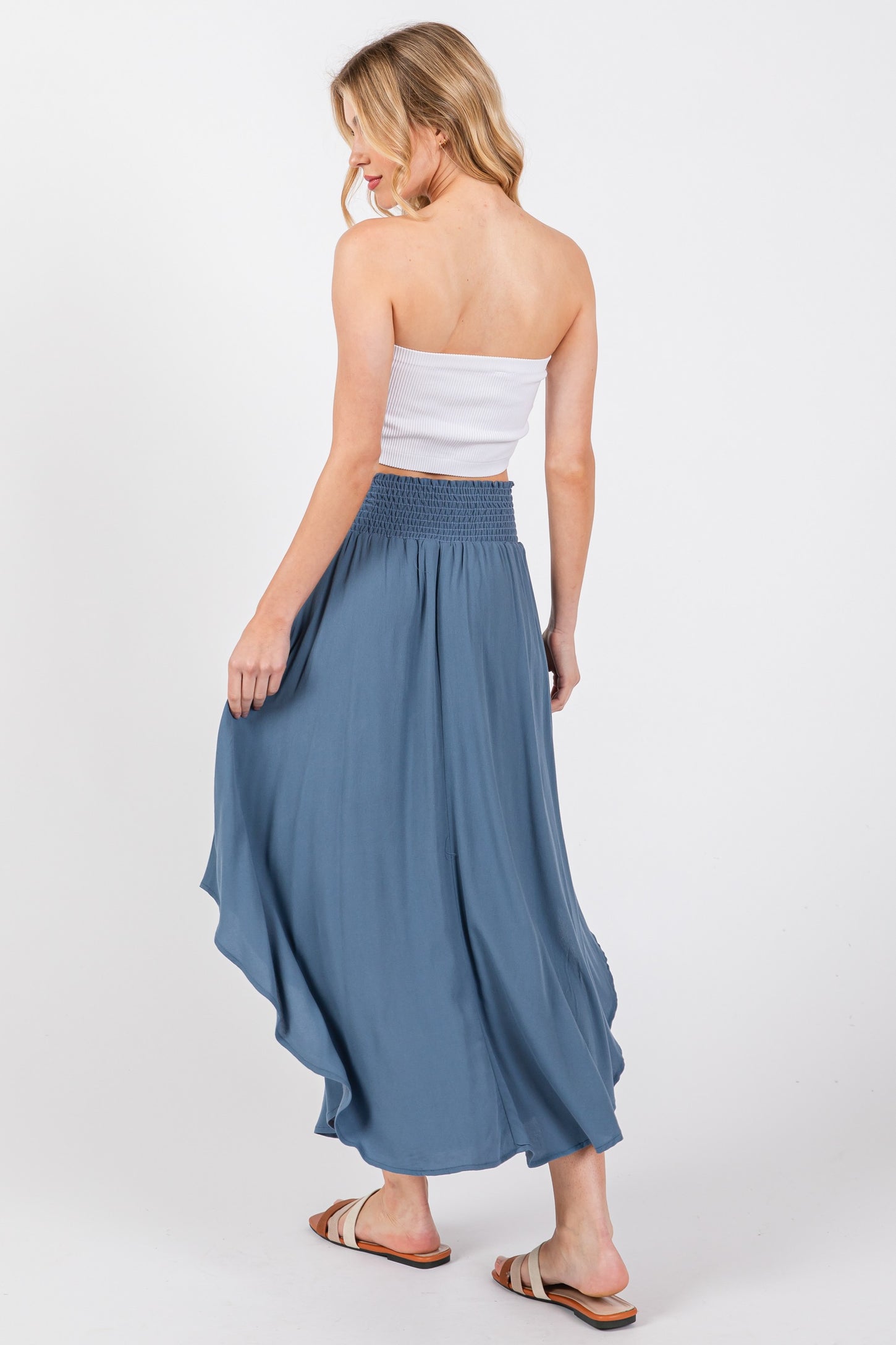 woman wearing a white strapless top and a flowing blue maxi skirt, viewed from the back