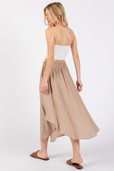 woman wearing a white spaghetti strap top and a beige flowy maxi skirt, standing with her back to the camera