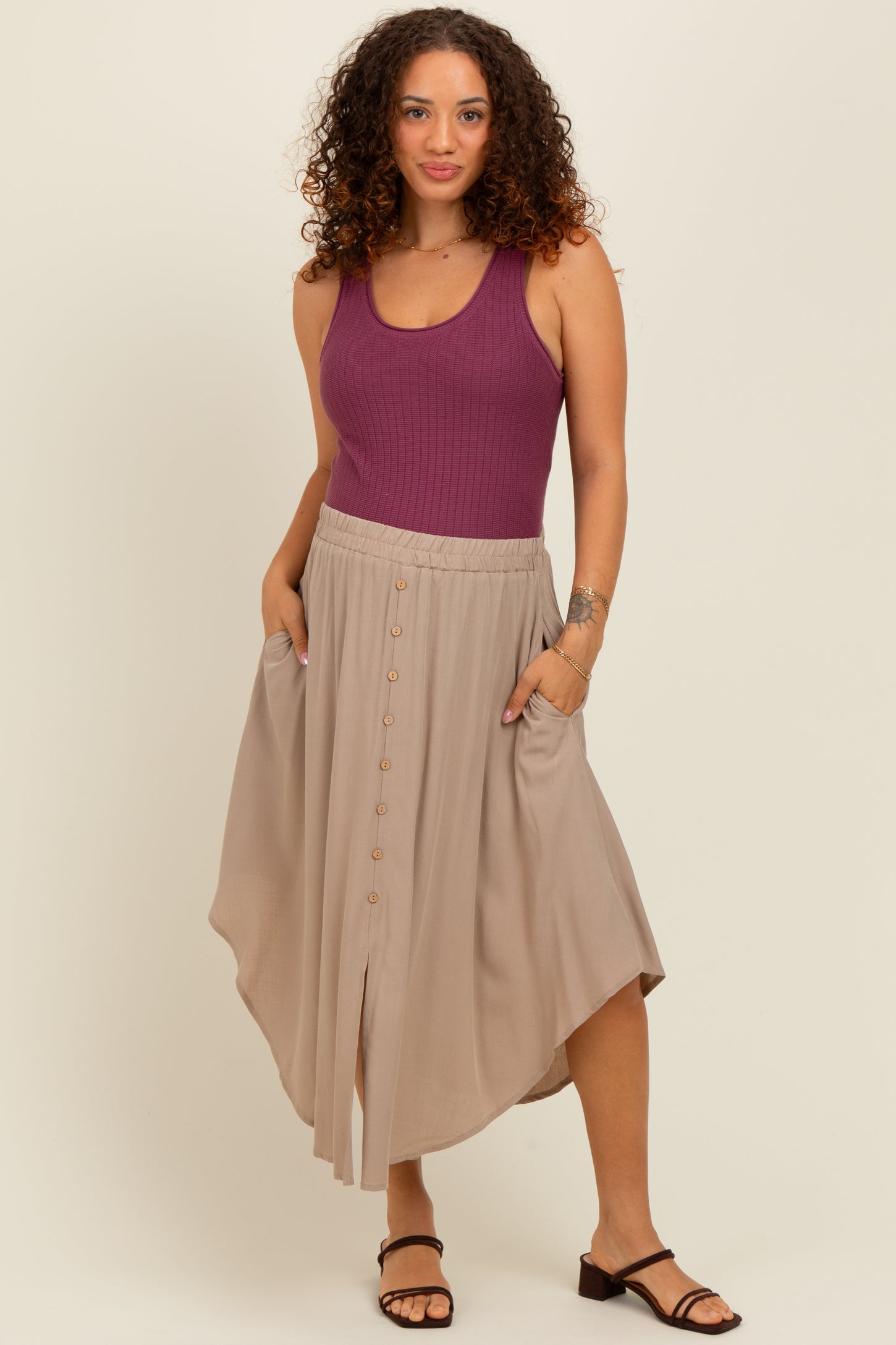 woman wearing a purple ribbed tank top and a beige maternity skirt with buttons and pockets