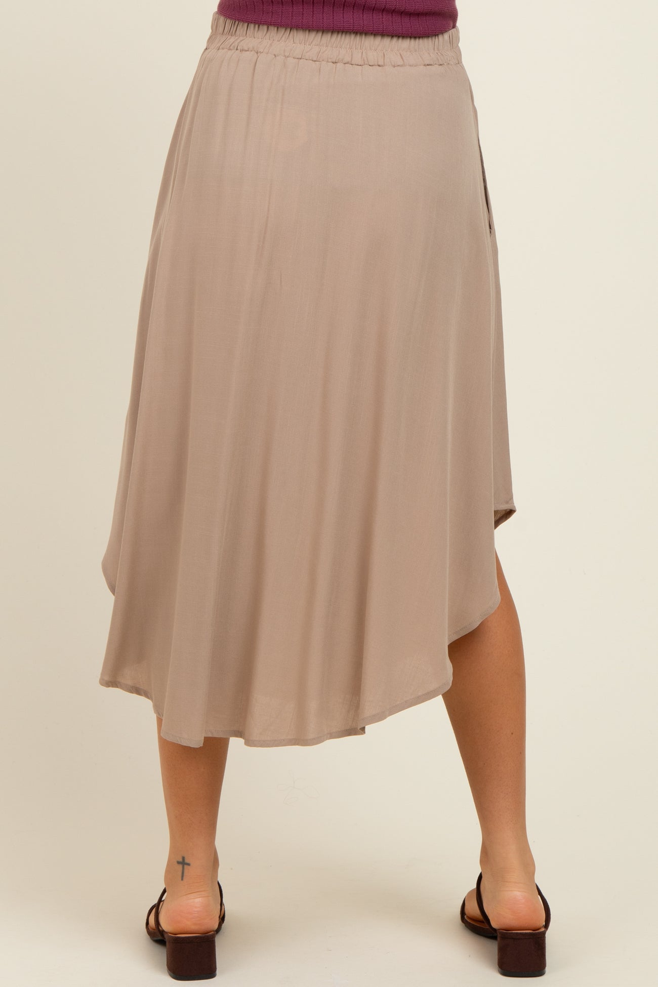 woman wearing a beige maternity skirt with an asymmetrical hem and elastic waistband, standing with her back to the camera