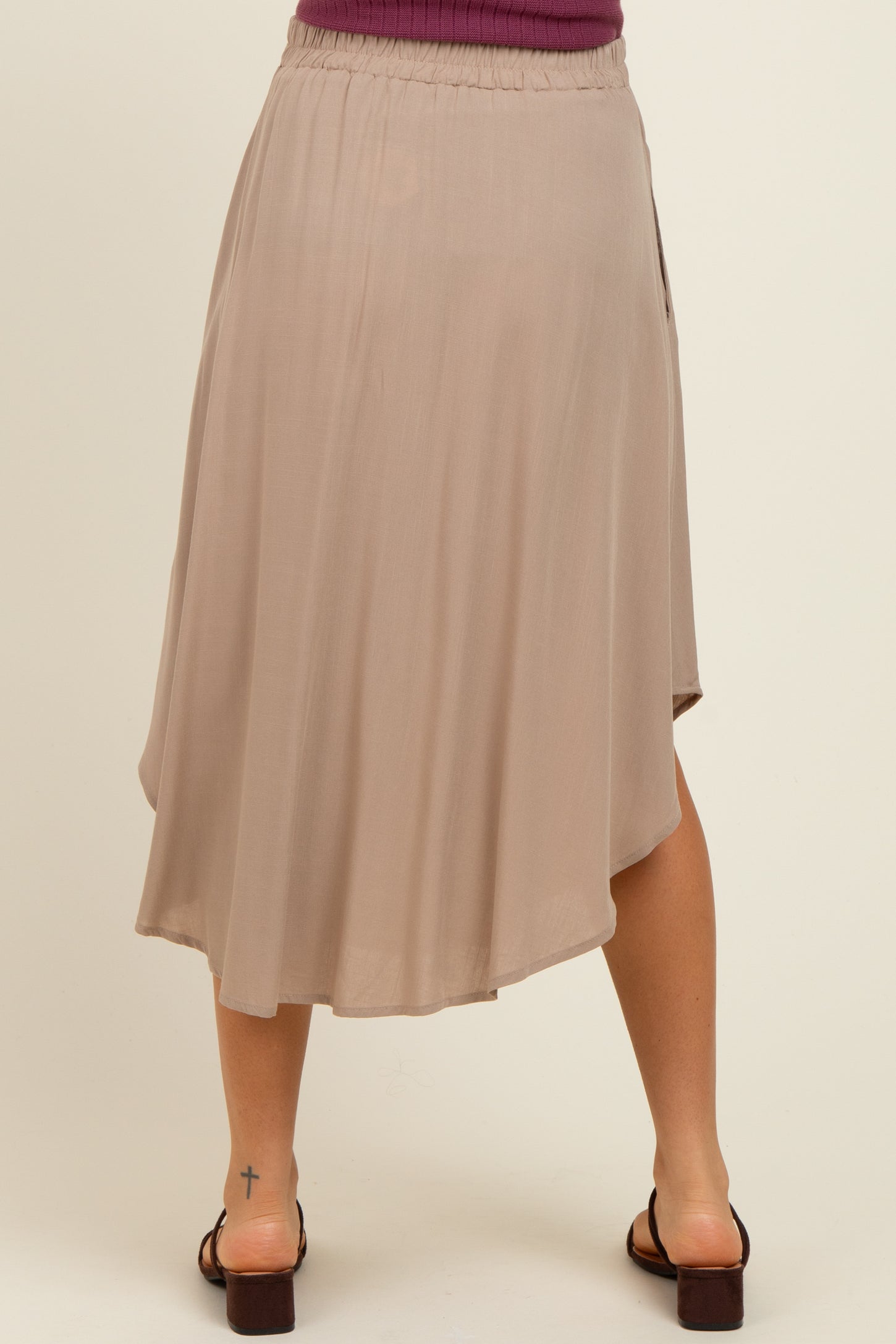 woman wearing a beige maternity skirt with an asymmetrical hem and elastic waistband, standing with her back to the camera