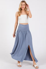 woman wearing a light blue maxi skirt with a front slit and a white cropped top, standing with one hand raised