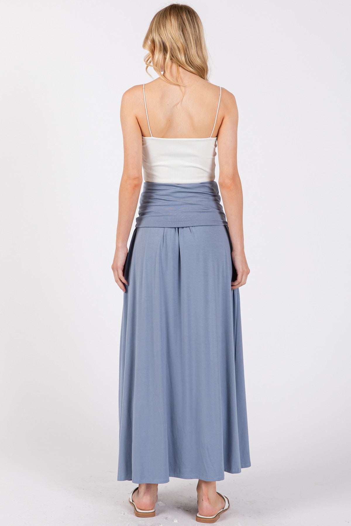 woman wearing a white camisole with a flowy blue maxi skirt, viewed from the back