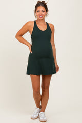 woman wearing a dark green maternity tank dress and showing her baby bump, paired with white sneakers