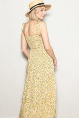 woman wearing a yellow floral maxi dress with shoulder ties and straw hat, turned to show the back view
