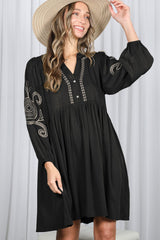woman wearing a black long sleeve dress with embroidered details and a button front, accessorized with a wide-brimmed hat