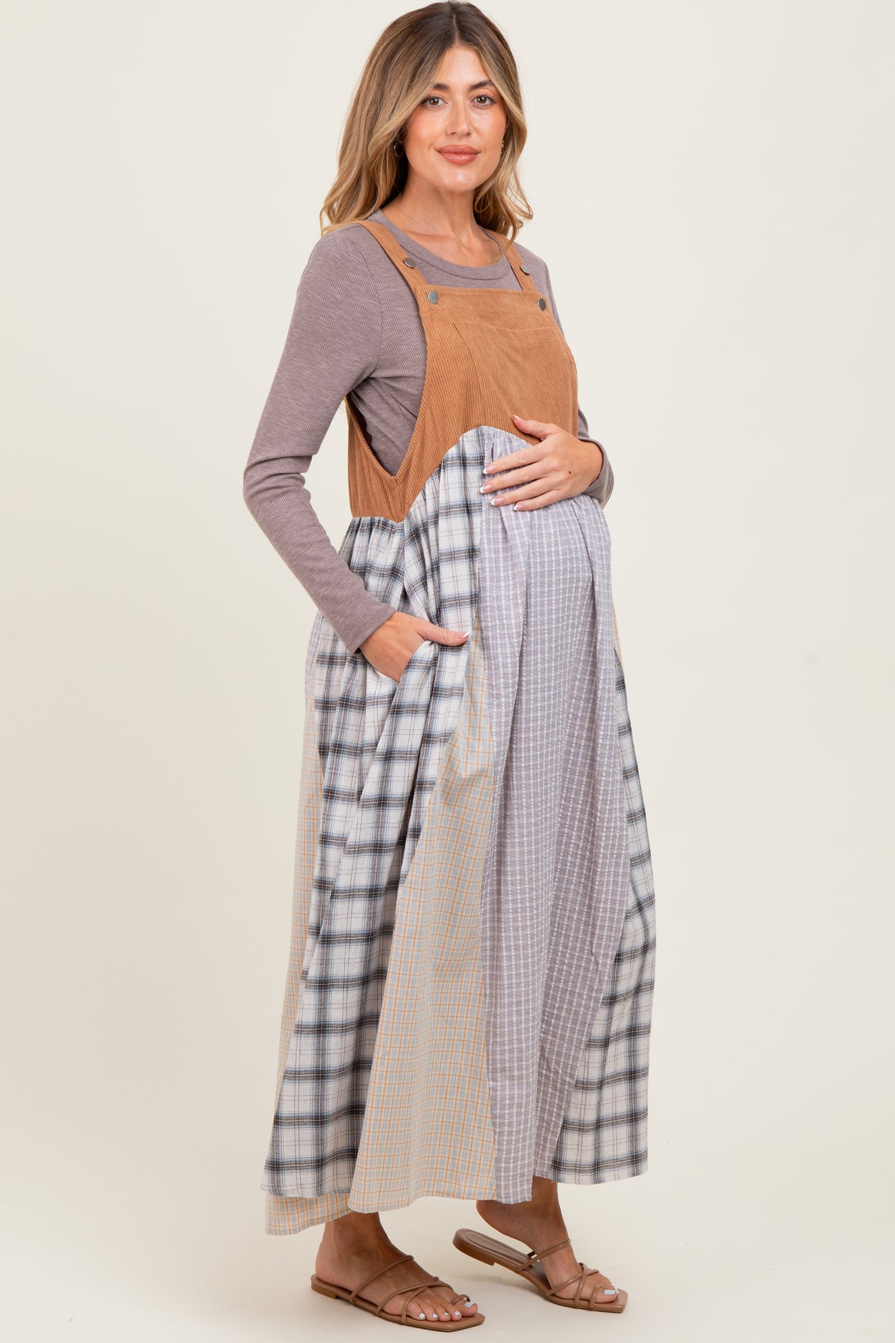 woman wearing a tan corduroy maternity dress with plaid patterns and pockets, showing her baby bump
