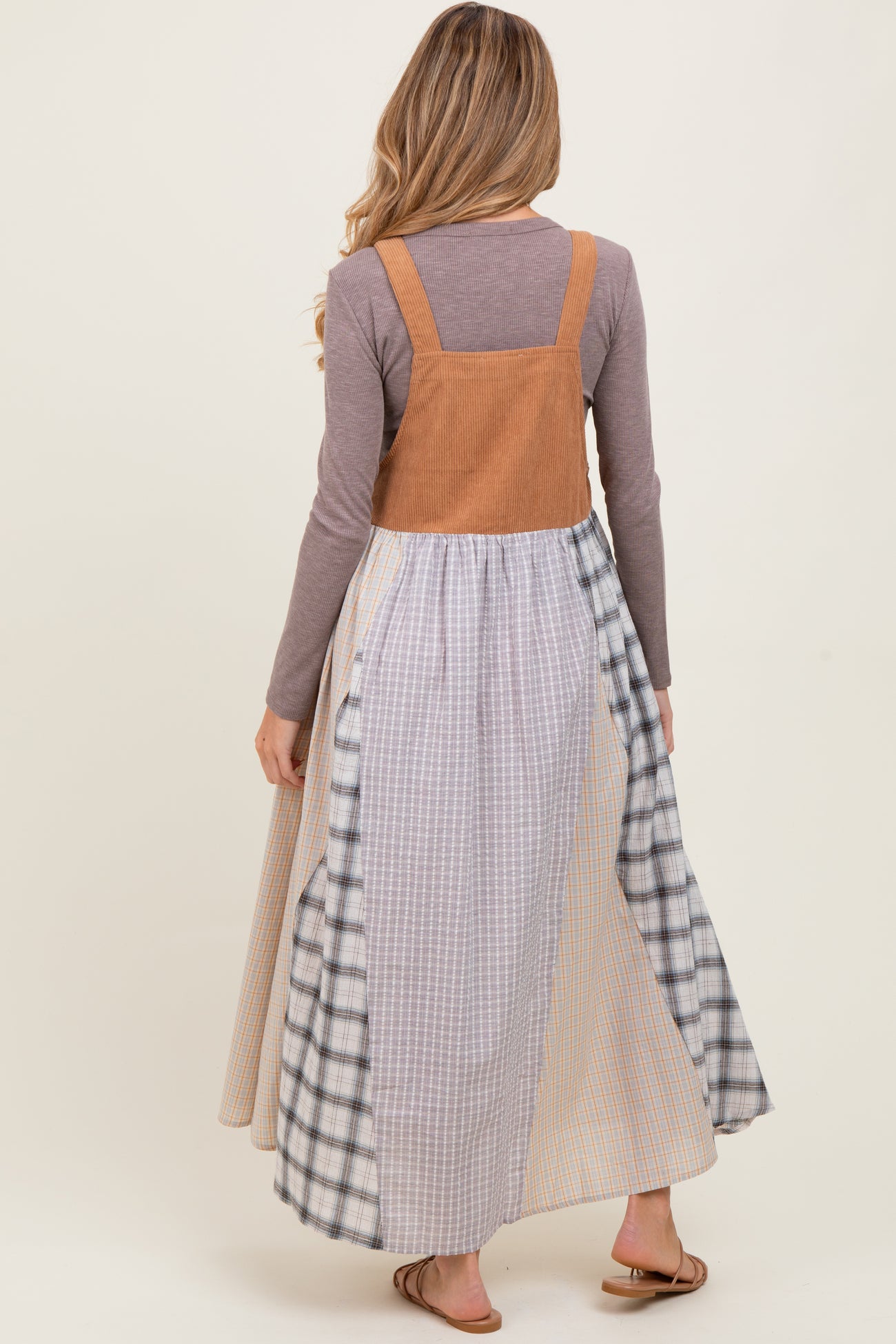woman wearing a brown corduroy maternity dress with a long plaid skirt, viewed from the back