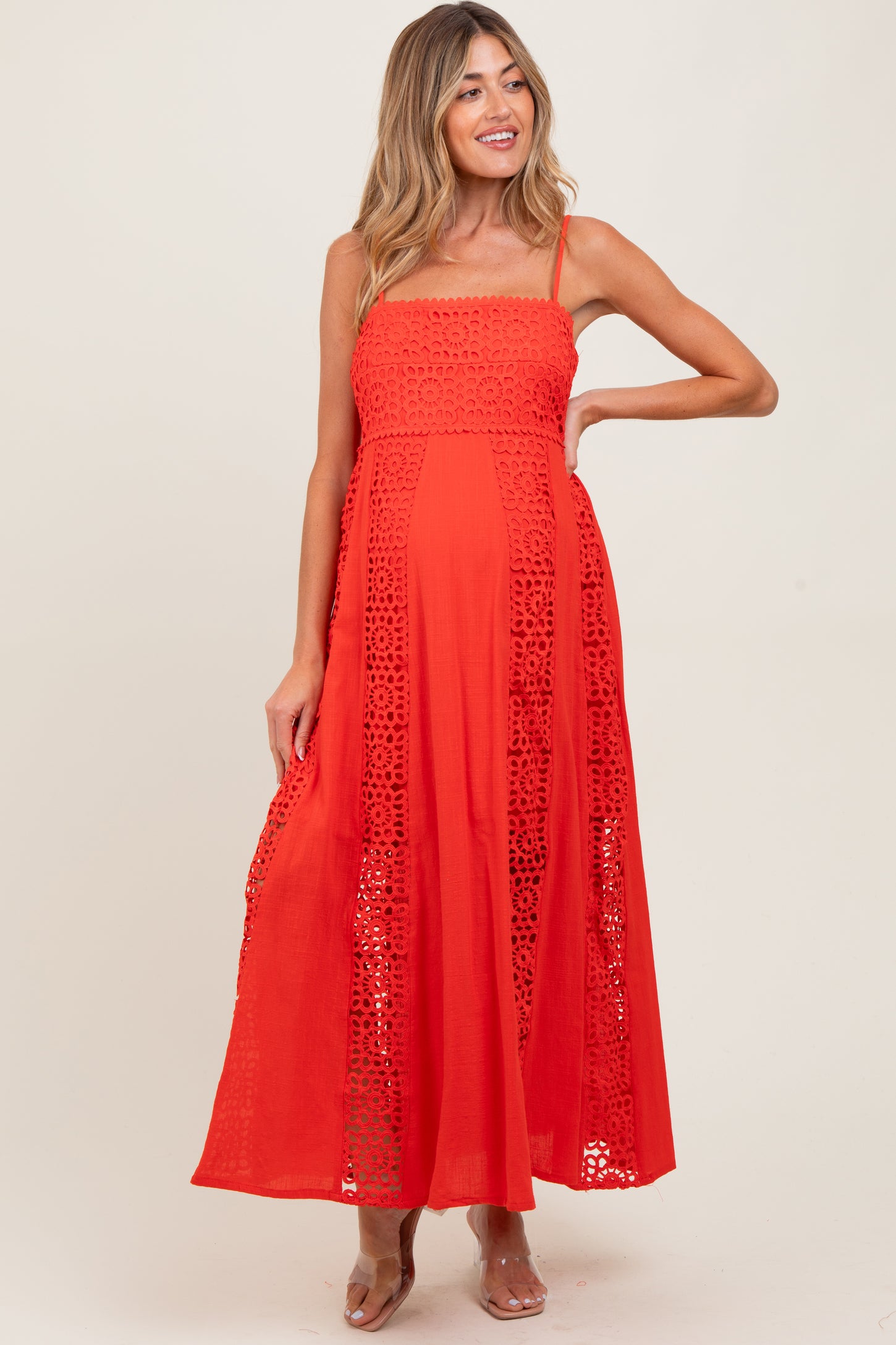 woman wearing a bright red maternity maxi dress with lace details and adjustable straps, showcasing her baby bump