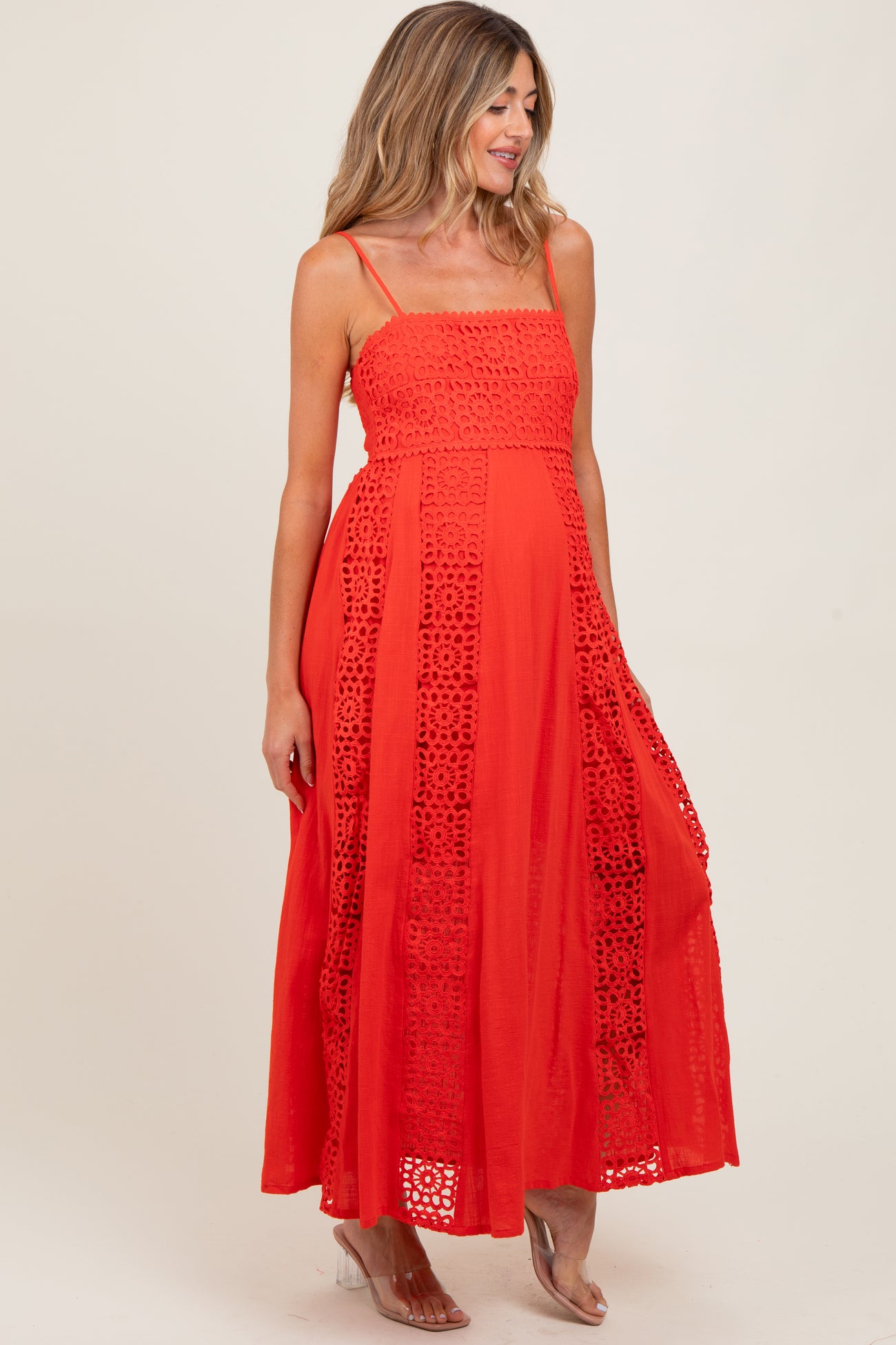 woman wearing a bright red maxi maternity dress with lace details and spaghetti straps, showcasing her baby bump