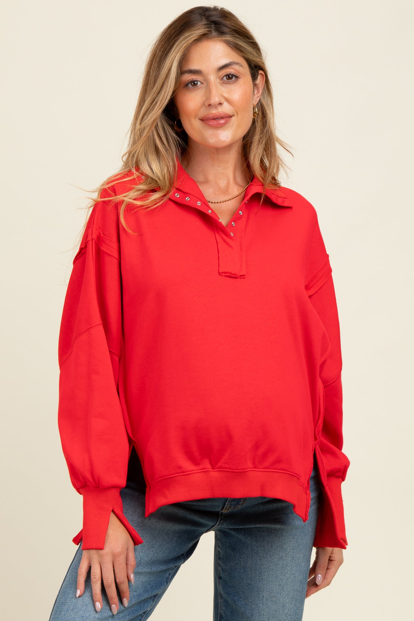 woman wearing a bright red maternity pullover with a collar and button detail, styled with casual jeans