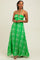 woman wearing a green maxi dress with white floral patterns and a halter neckline, standing against a neutral background