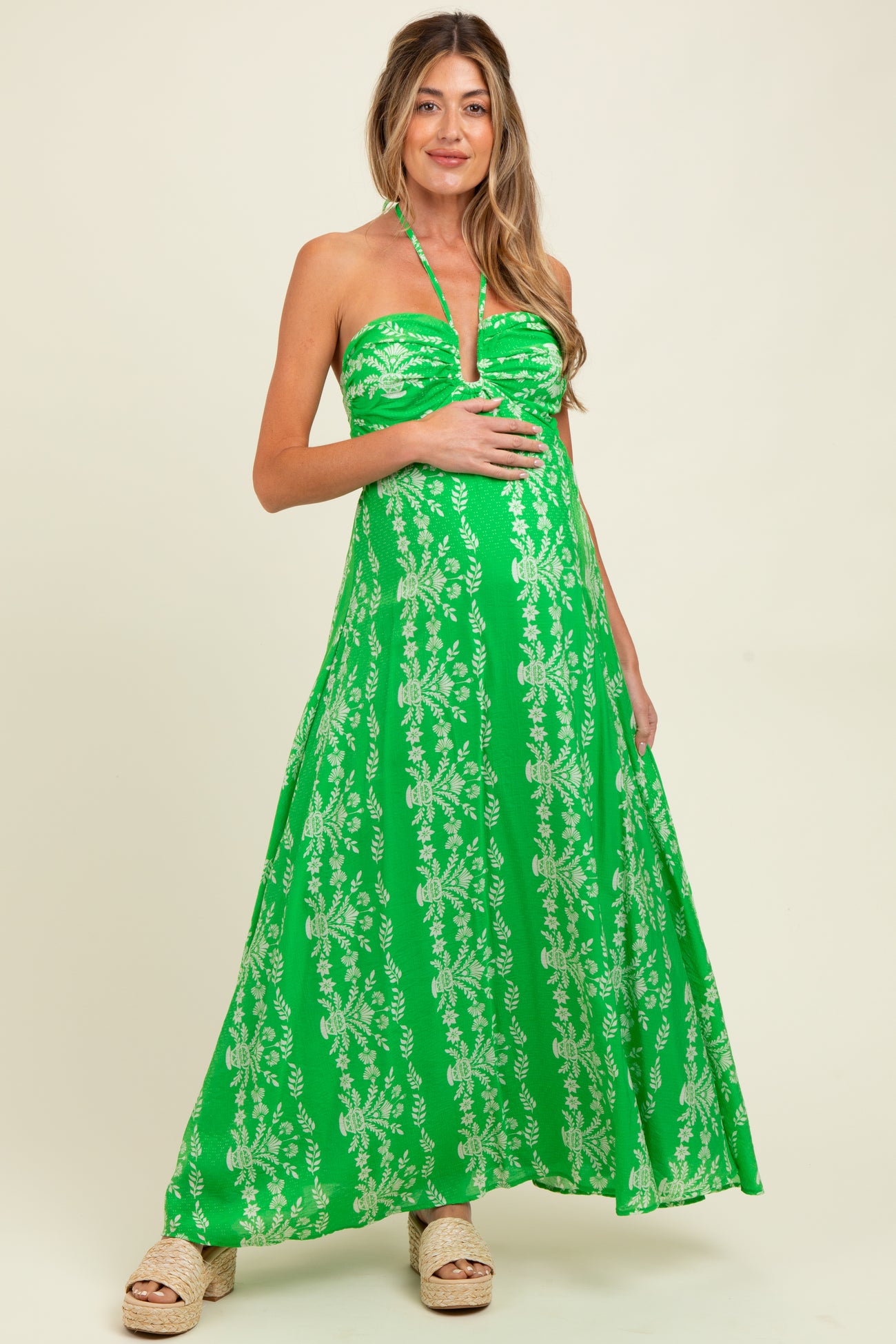 woman wearing a green strapless maxi dress with floral patterns and holding her baby bump