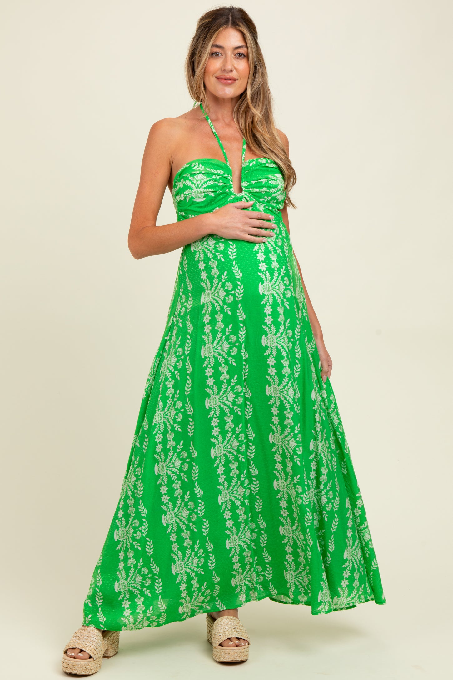 woman wearing a green strapless maxi dress with floral patterns and holding her baby bump
