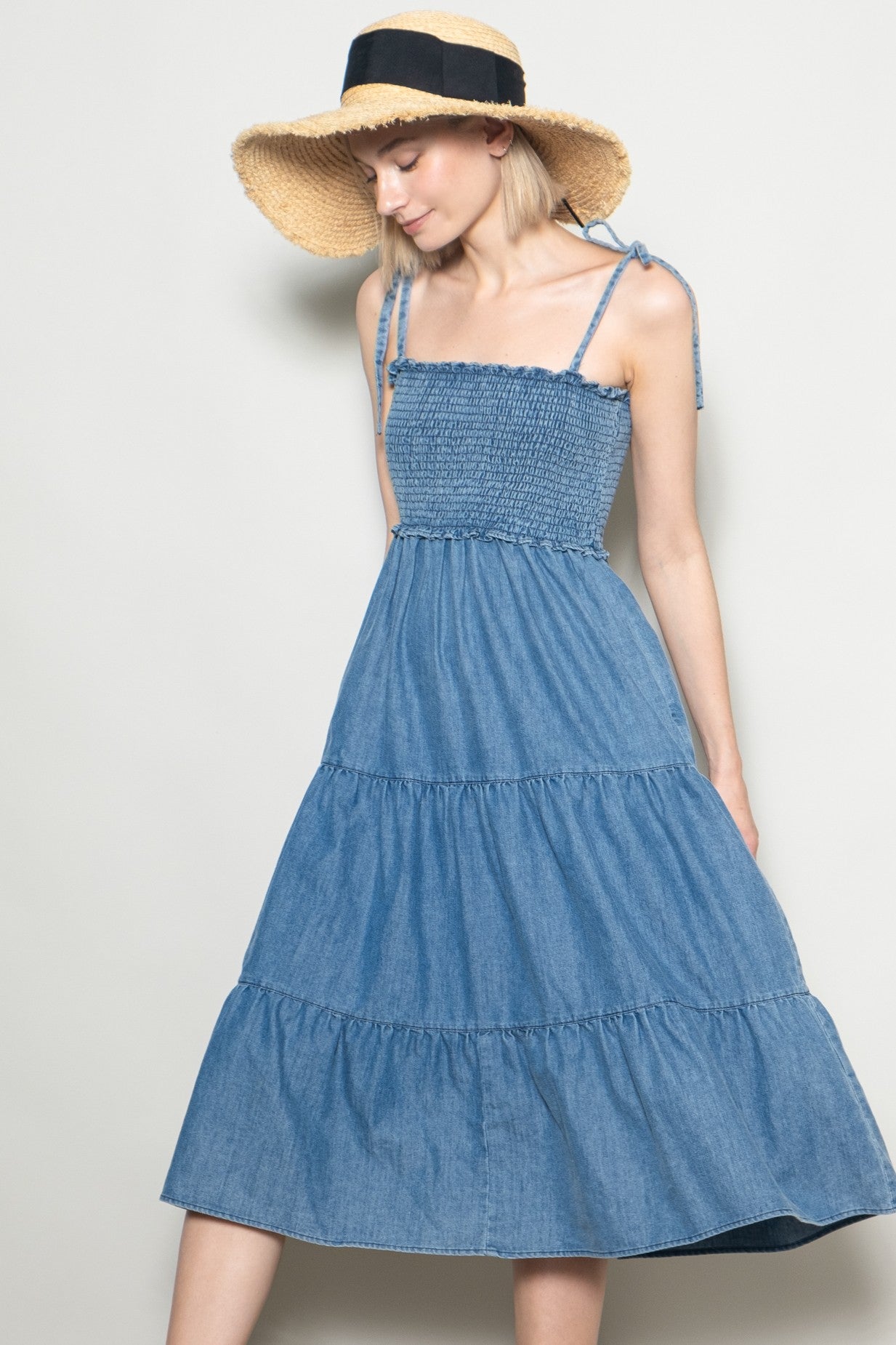 woman wearing a blue denim sundress with spaghetti straps and a tiered skirt, paired with a wide-brim straw hat