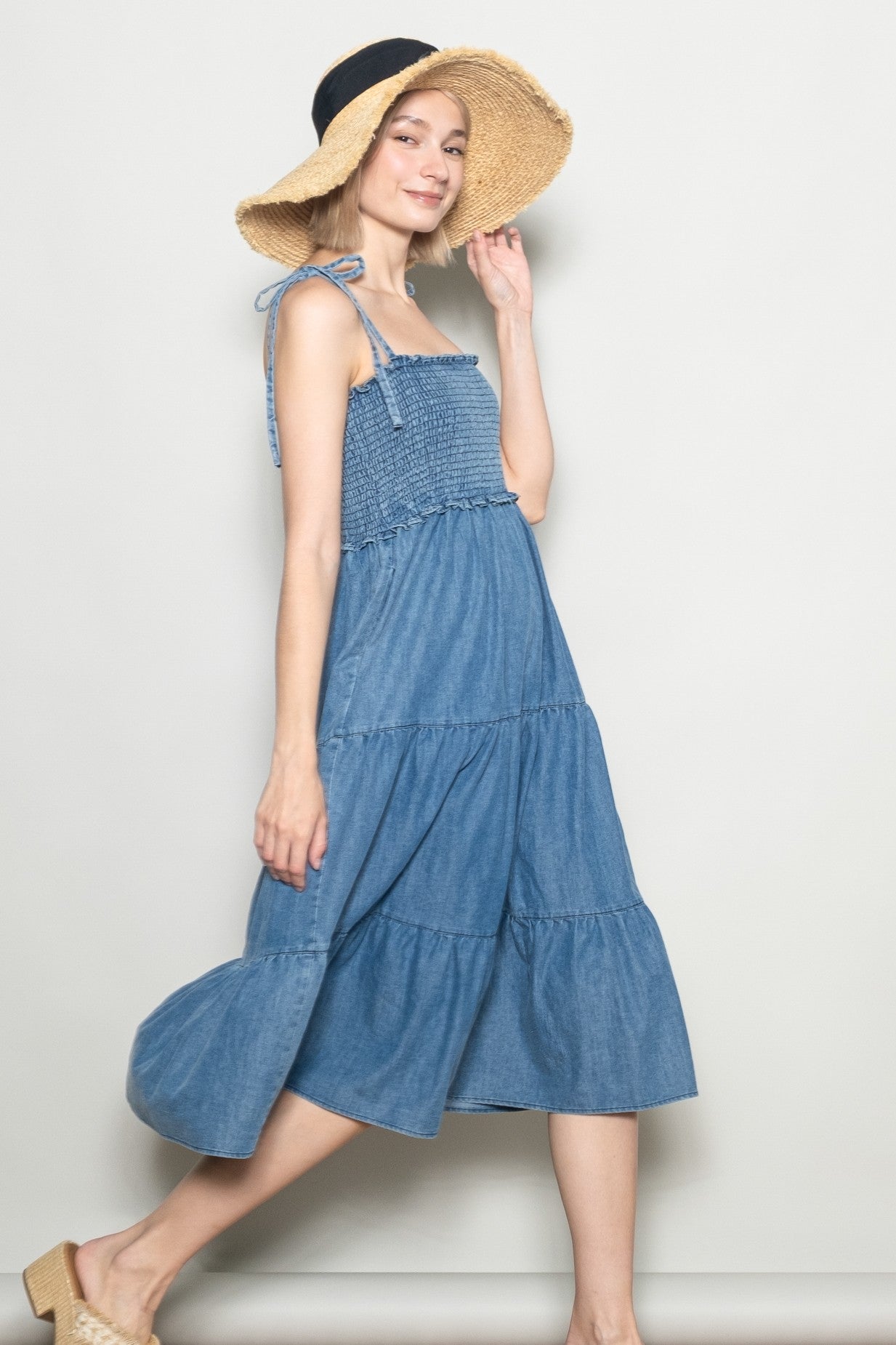 woman wearing a sleeveless denim tiered midi dress with a smocked bodice and a wide-brim straw hat