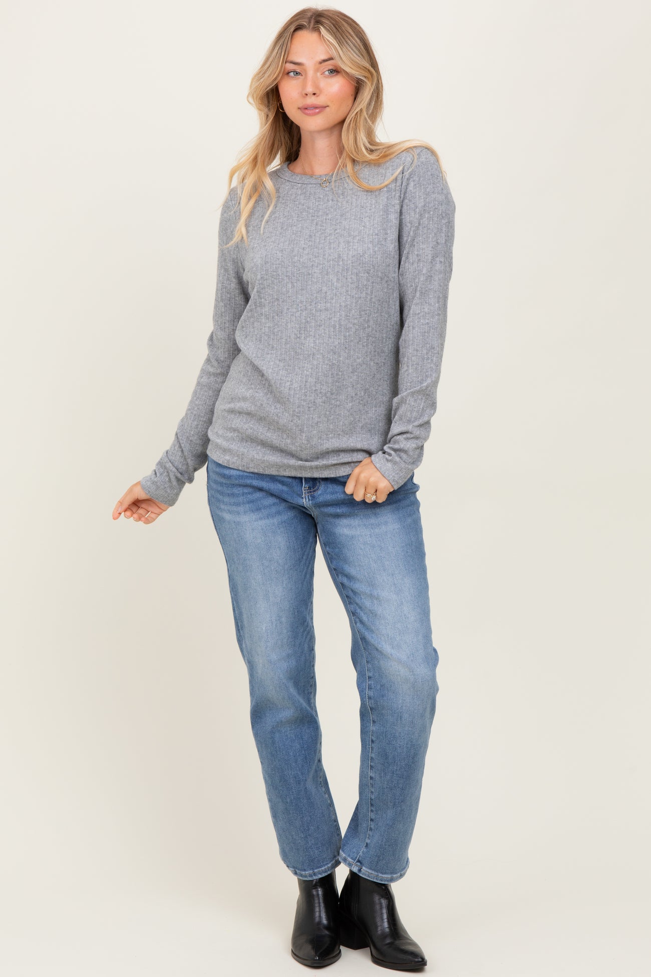 woman wearing a gray long sleeve ribbed top and blue jeans, posed with one hand on her hip
