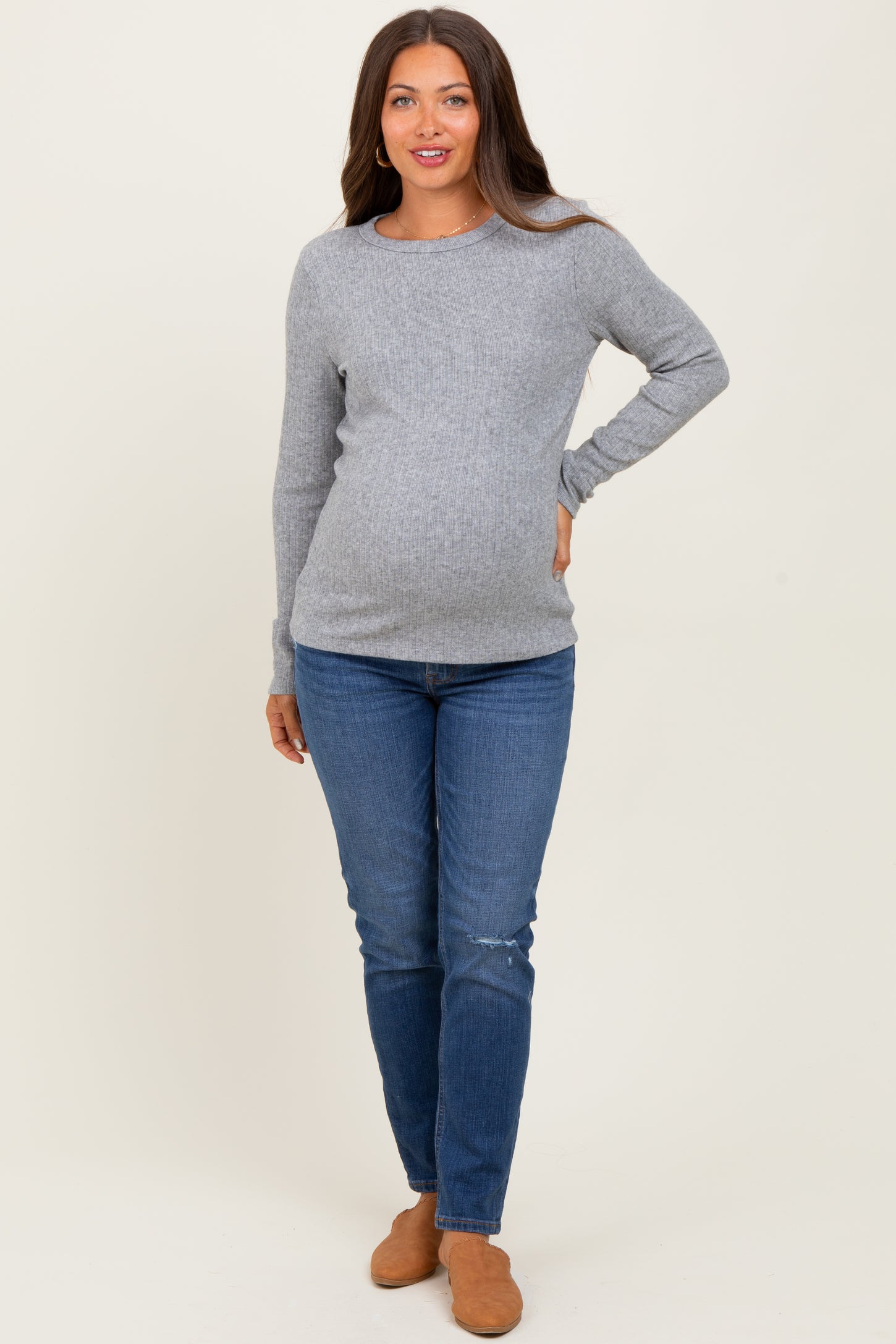 woman wearing a light gray long sleeve maternity top and blue skinny jeans showing her baby bump