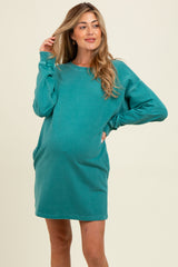 woman wearing a teal maternity sweatshirt dress with side pockets and a visible baby bump
