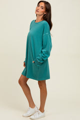 woman wearing a teal oversized sweatshirt dress with long sleeves and side pockets, styled with white sneakers