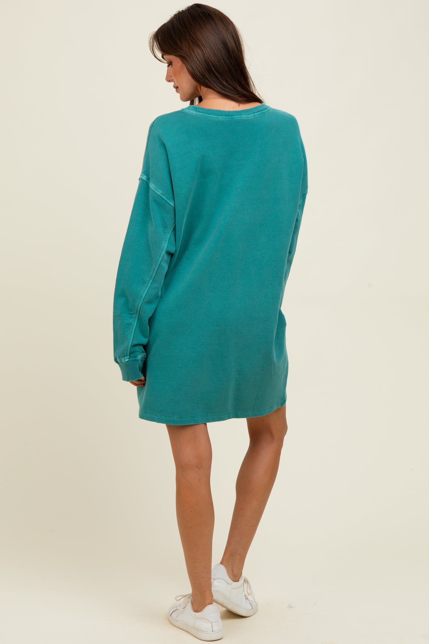 woman wearing a teal oversized sweatshirt dress, featuring long sleeves and a relaxed fit, standing with her back to the camera