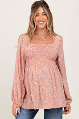 woman wearing a dusty rose floral maternity blouse with balloon sleeves and a smocked bodice, showing her baby bump