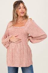 woman wearing a rust floral maternity top with puff sleeves and a gathered waist, holding her baby bump