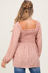 woman wearing a coral floral maternity top with a smocked back and long sleeves, showing her baby bump