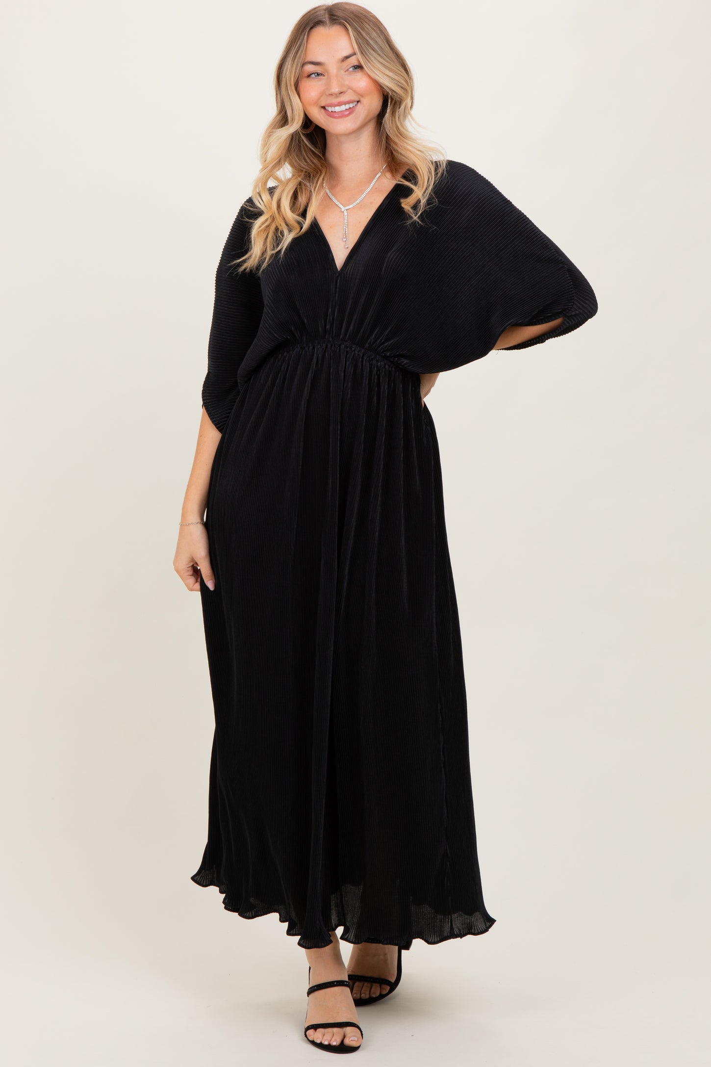woman wearing a black maxi dress with a deep v-neck and cinched waist, smiling and posing against a light background