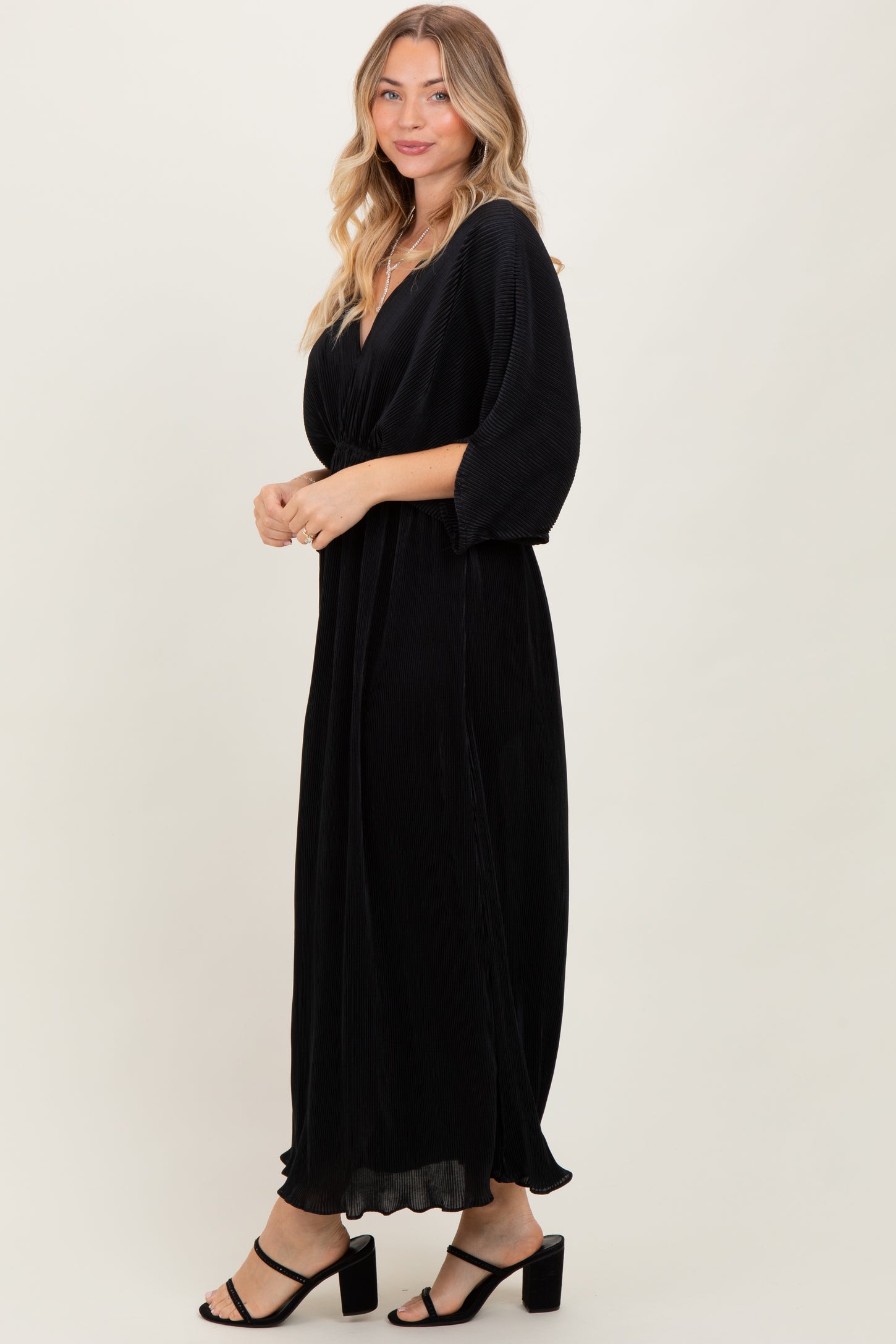 woman wearing a black maxi dress with a deep v-neck and puff sleeves, styled with strappy black heels
