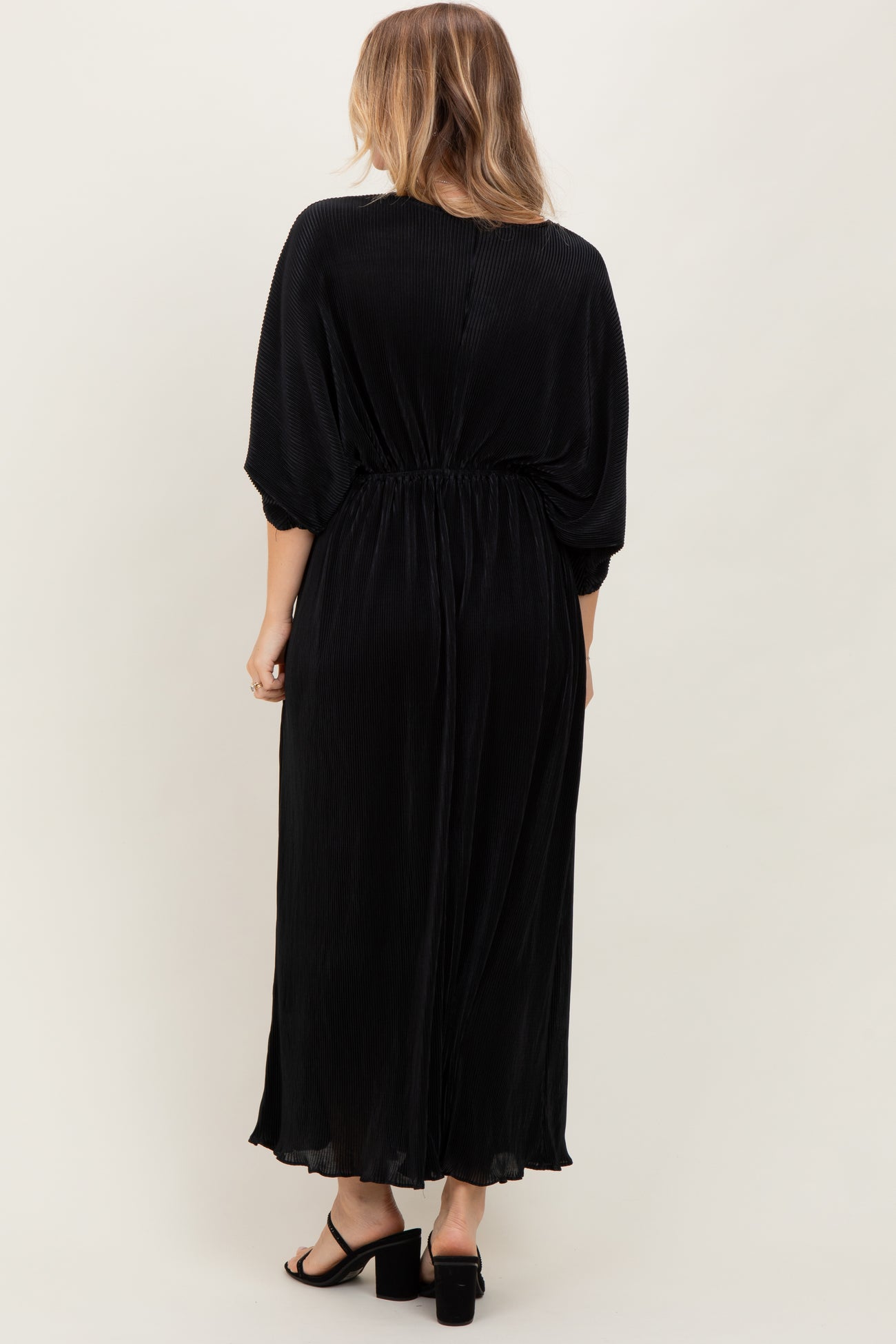woman wearing a black pleated maxi dress with a cinched waist and flowing sleeves, shown from the back