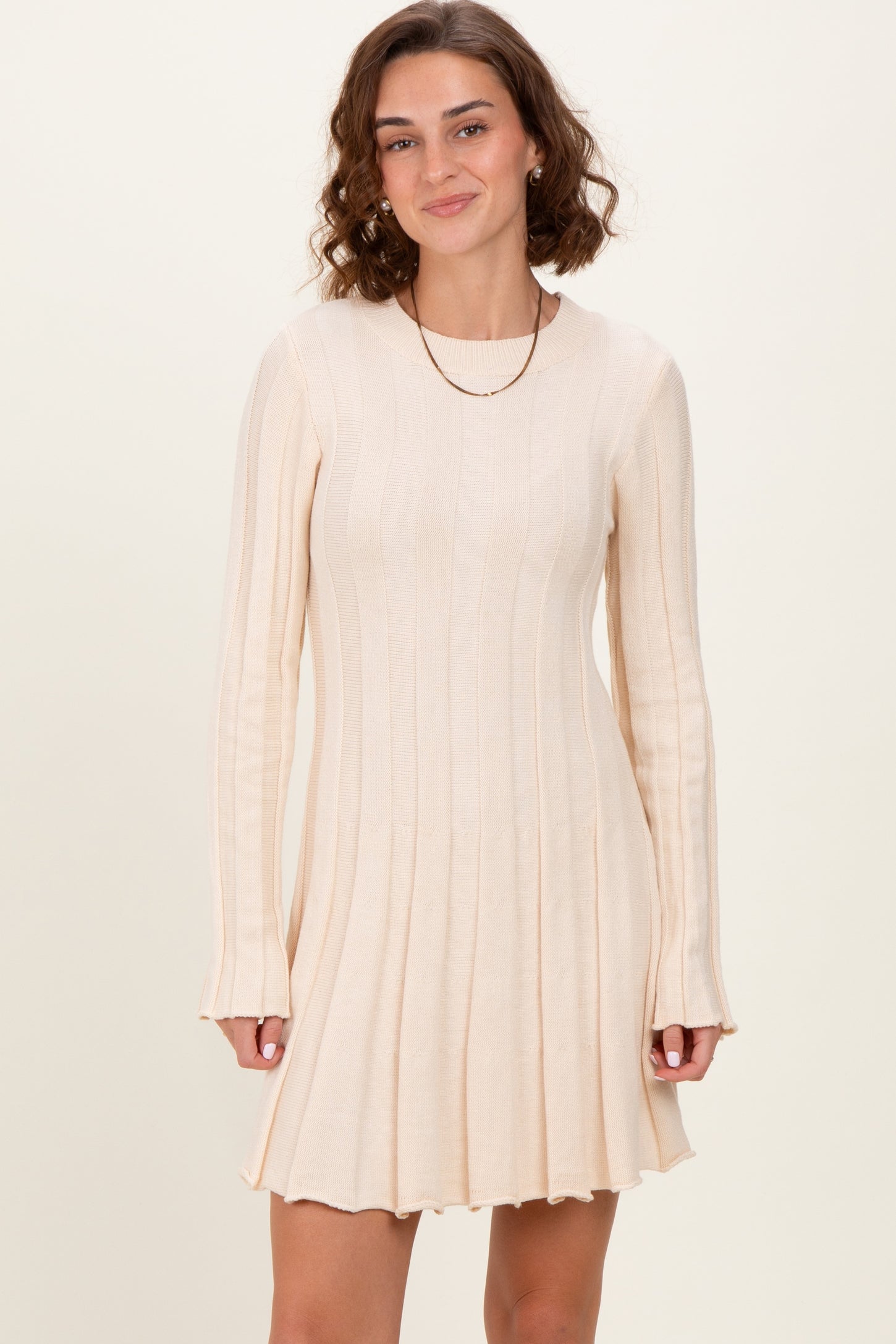 woman wearing a light beige ribbed long sleeve dress with a flared skirt and flared cuffs